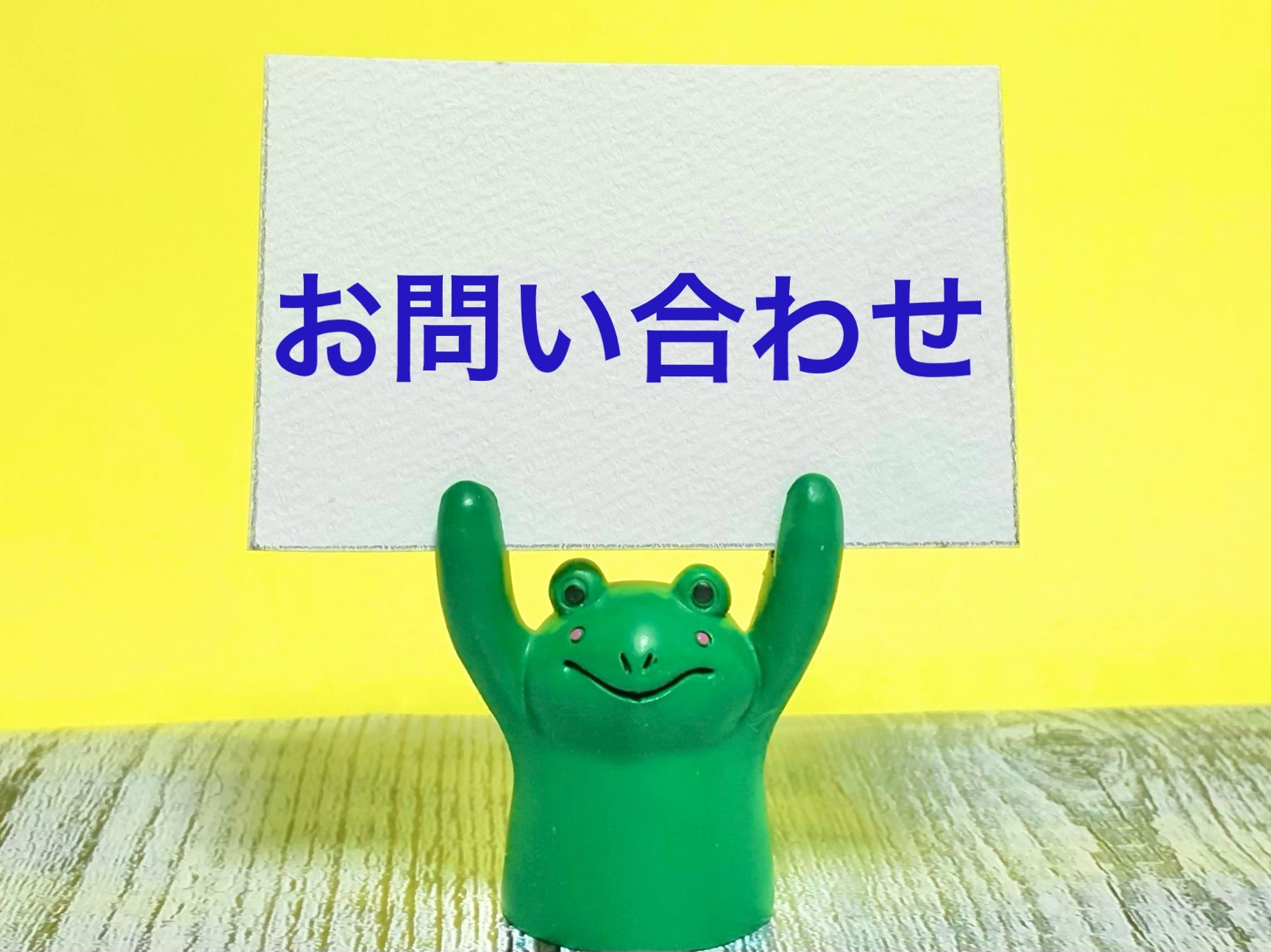 お問い合わせの札を掲げるカエル人形